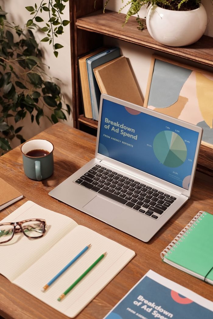 Our Services Laptop displaying ad spend data on a wooden desk with office supplies.